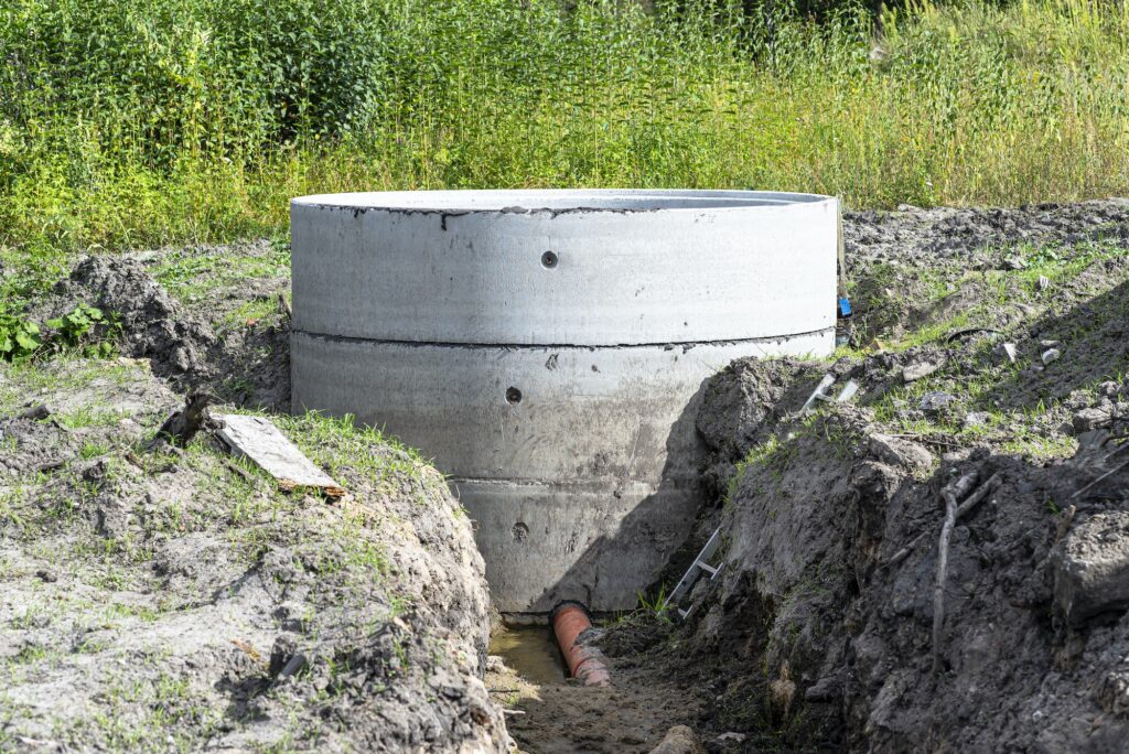 Concrete septic tank made of several rings with an orange drainpipe at the bottom.